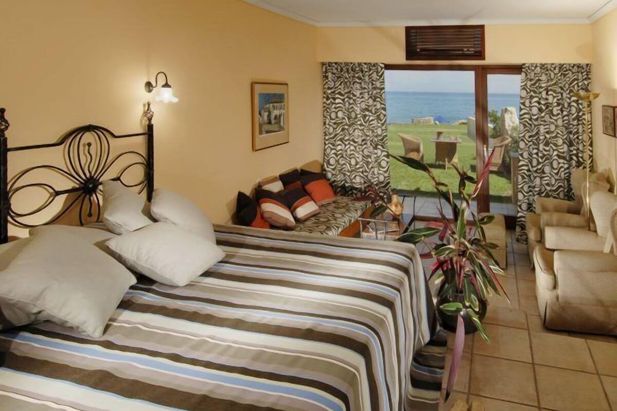 Ein Schlafzimmer mit Bett, Kissen, einer Couch, einem Sessel, einem Tisch und Meerblick.