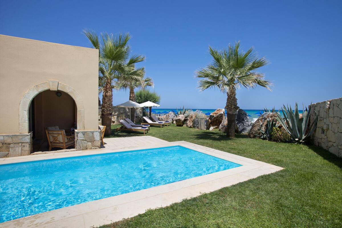 Ein Swimmingpool mit Liegestühlen, Palmen und Blick auf das Meer.