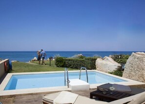 A pool area with a view of the ocean, a lounge chair, and a small table with a flower.