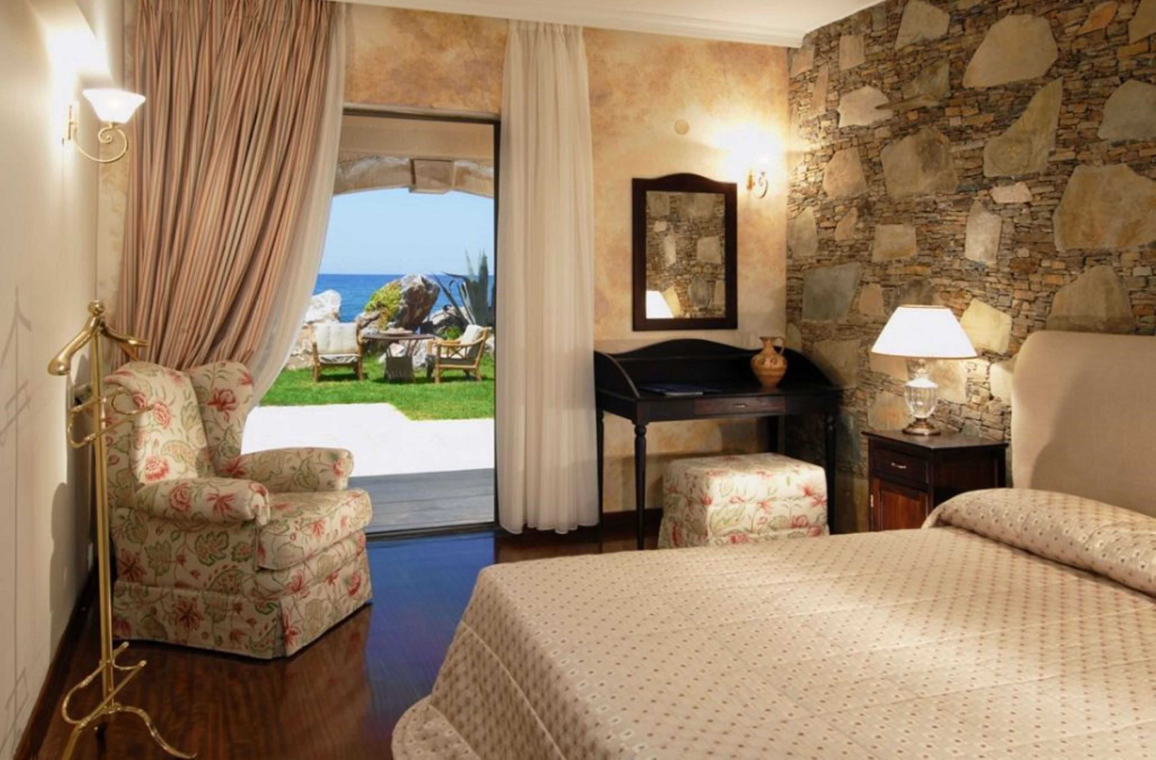 Een hotelkamer met een bed, een bureau, een stoel en uitzicht op zee.