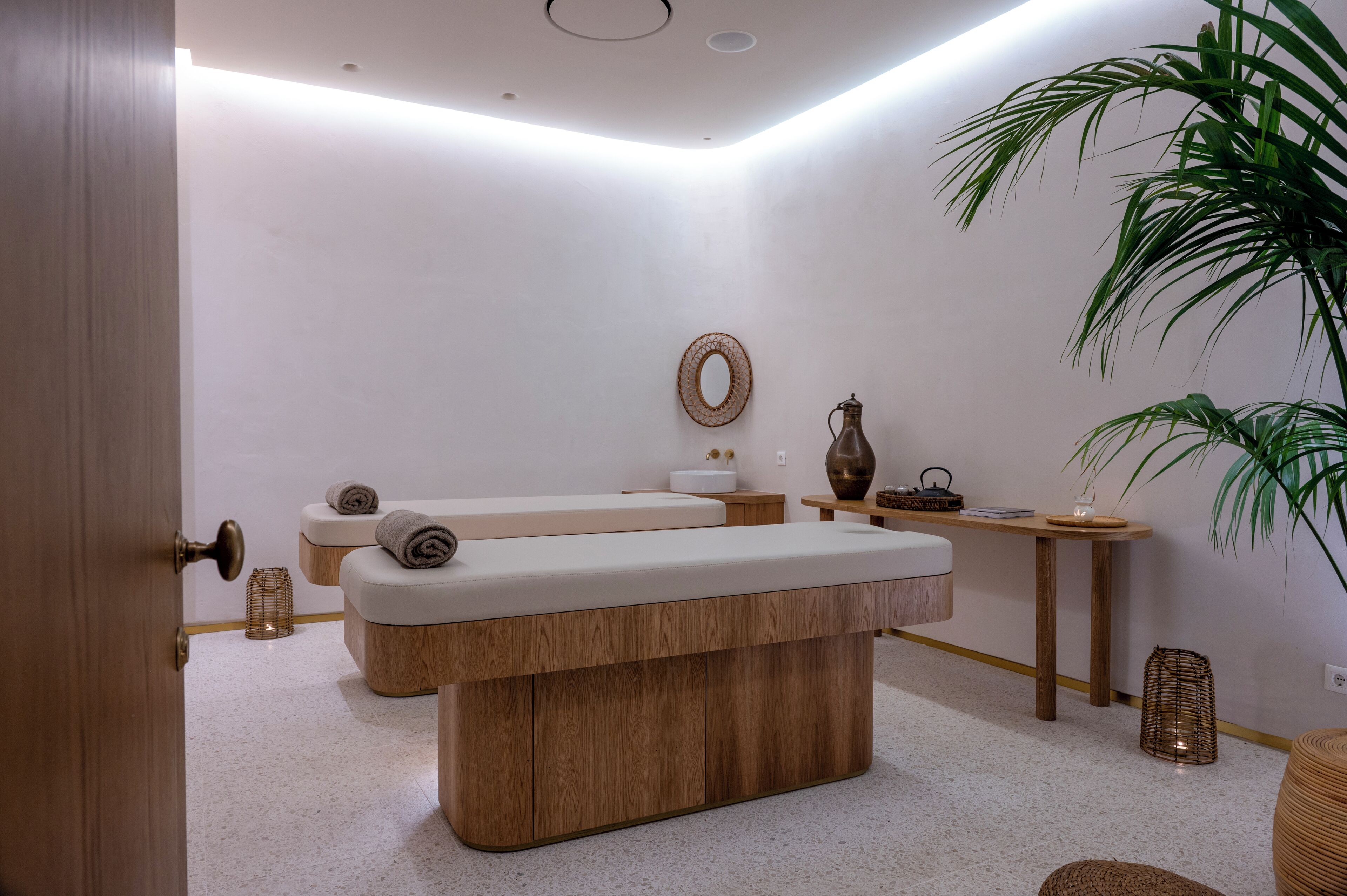 Een wellnessruimte met een houten bankje, een tafeltje met een vaas en een potplant.