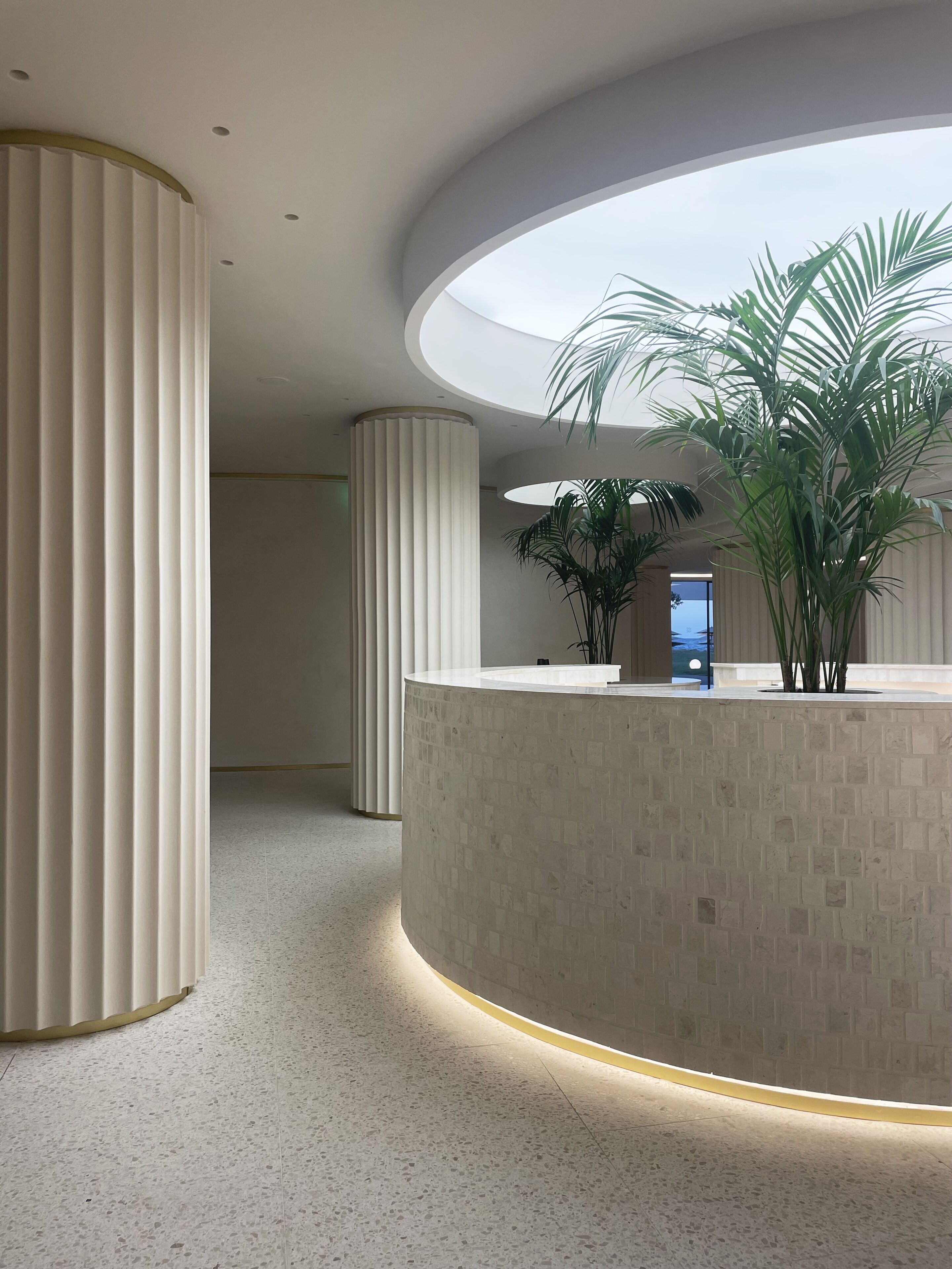 Un área de recepción moderna con un mostrador curvo, altas columnas cilíndricas y un tragaluz.