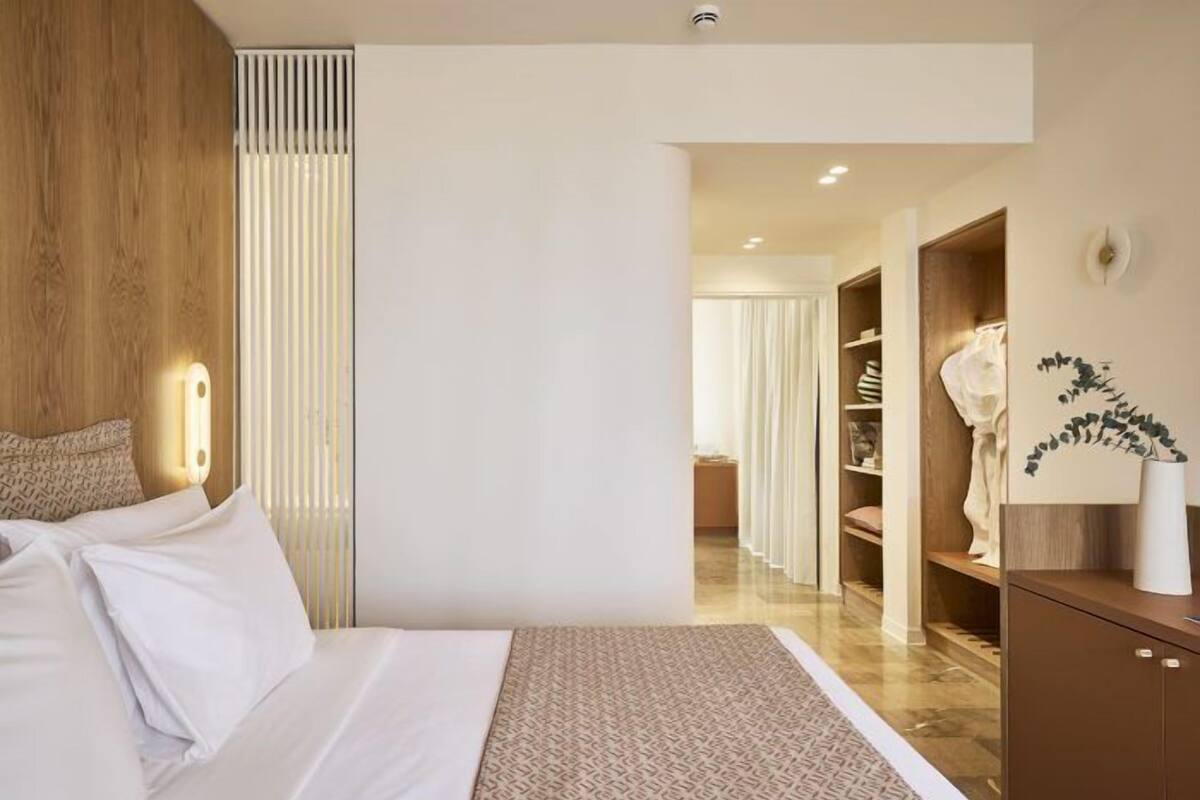Ein modernes Hotelzimmer mit einem großen Bett, einem Holz-Kopfstück, einer Nachttischlampe, einem gemusterten Teppich, einem Kleiderschrank und einem Spiegel.