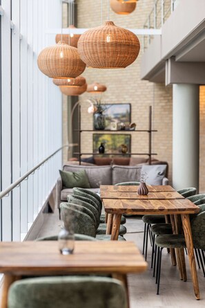 Een modern interieur met een houten tafel en stoelen, zittingen van riet en een bank met kussens.