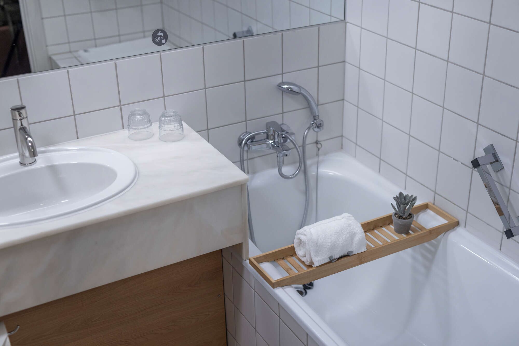 A bathroom with a sink, mirror, shower, and a towel rack.