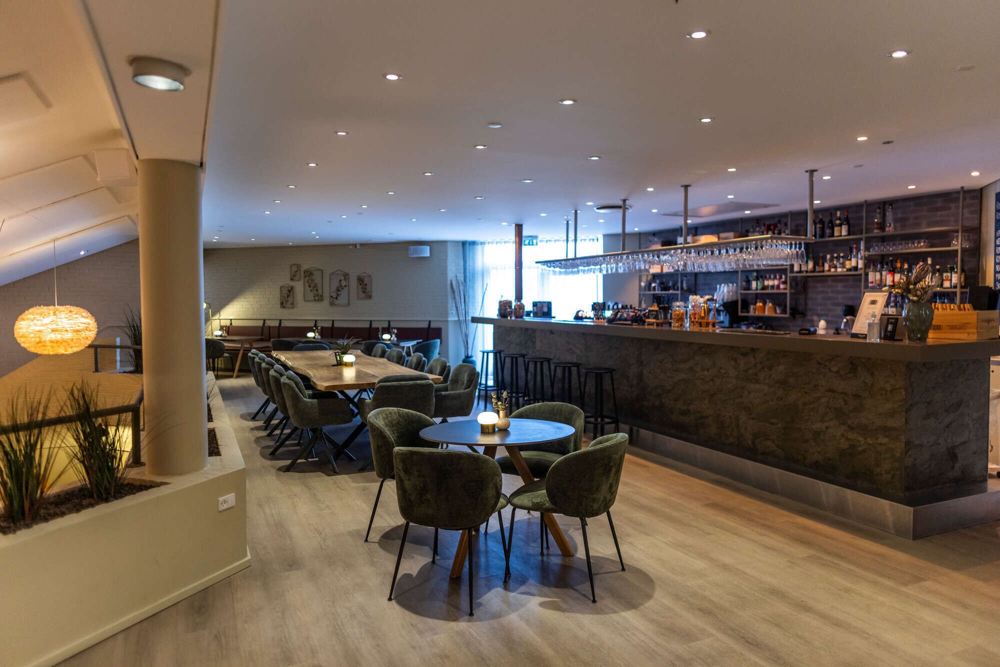 A modern bar area with a long counter, bar stools, and a variety of bottles and glasses.