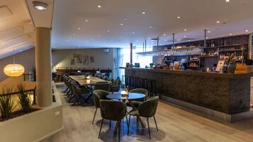 A modern bar area with a long counter, bar stools, and a variety of bottles and glasses.