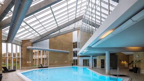 An indoor swimming pool with a glass ceiling, a brick wall, and a blue pool ladder. - Comwell Rebild Bakker (Skorping)