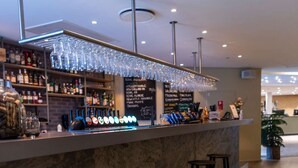 A bar area with a marble counter, multiple stools, and a selection of bottles and glasses. - Comwell Rebild Bakker (Skorping)