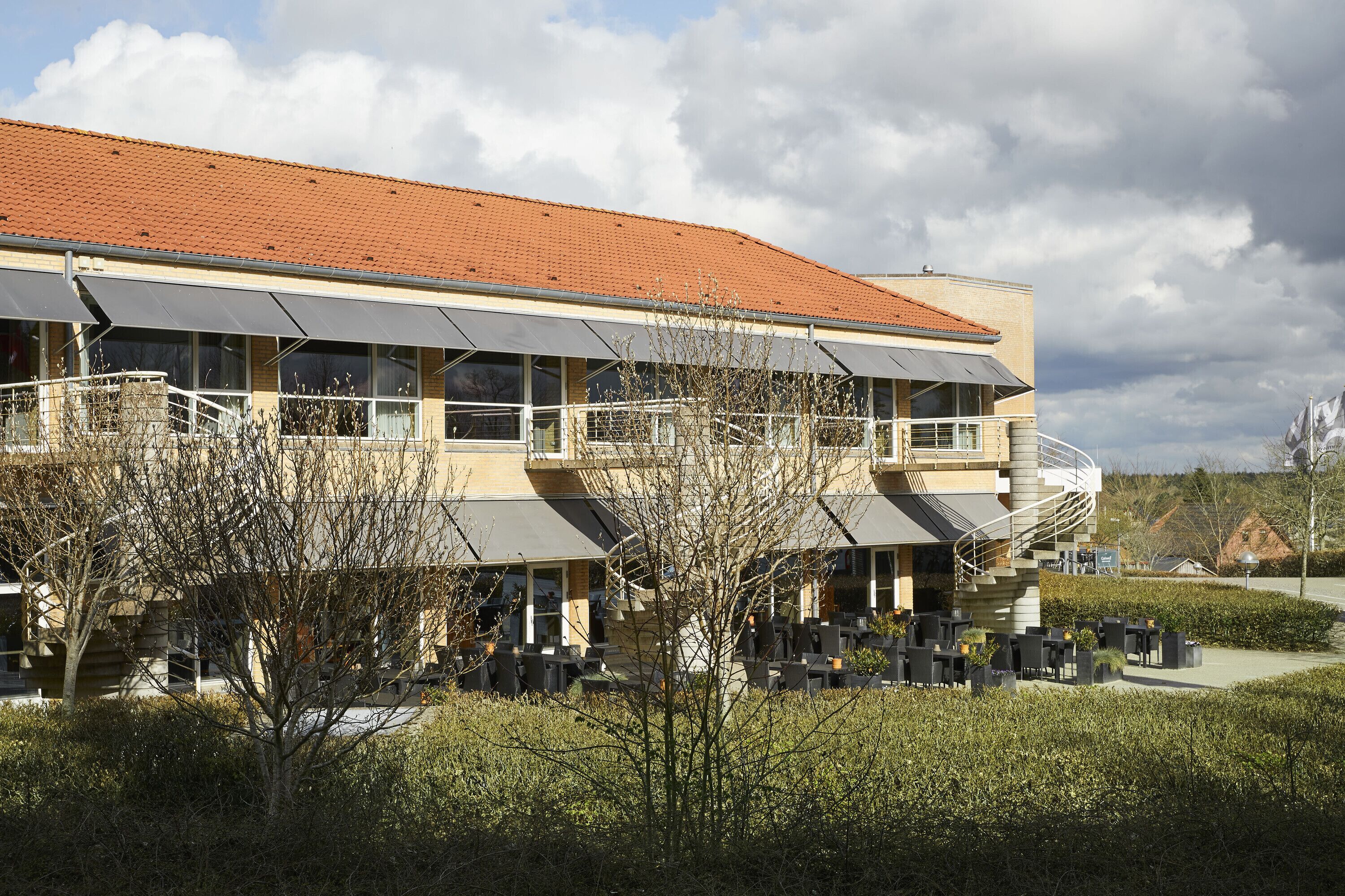 A modern building with a red-tiled roof, large windows, and outdoor seating areas.