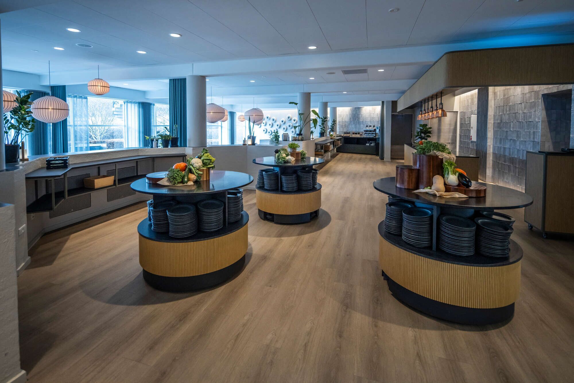 A modern restaurant interior with round tables, wooden flooring, and large windows.
