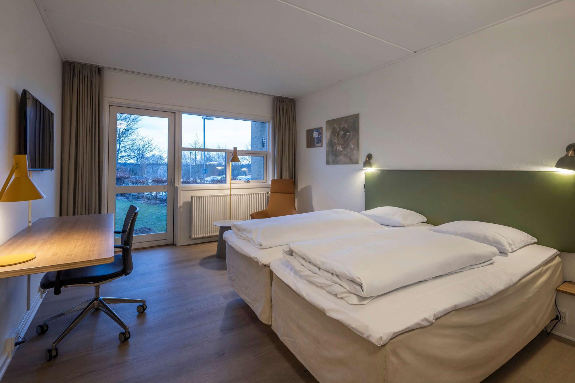 A hotel room with a bed, a desk, a chair, and a window.