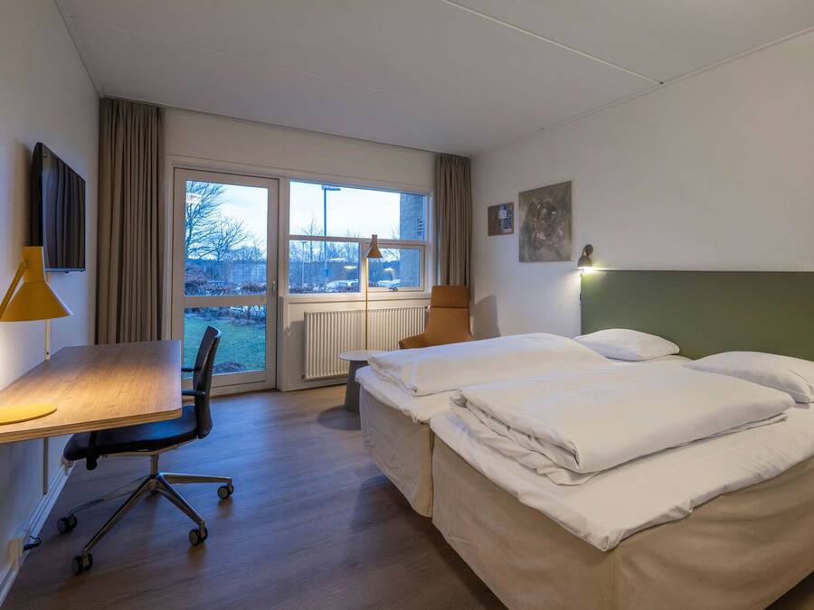 A hotel room with a bed, a desk, a chair, and a window.