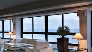 A modern hotel lobby with a large window overlooking the sea, a white sofa set, a coffee table, and a potted plant. - Grand Hotel Terme (Margherita di Savoia)