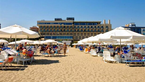 A beach with rows of sunbeds and umbrellas, a building in the background, and clear skies. - Grand Hotel Terme (Margherita di Savoia)