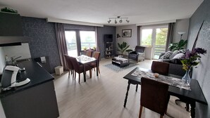 A modern living room with a dining area, a sofa, a coffee table, and a TV. - Blue Mountain Hotel (Treffen)