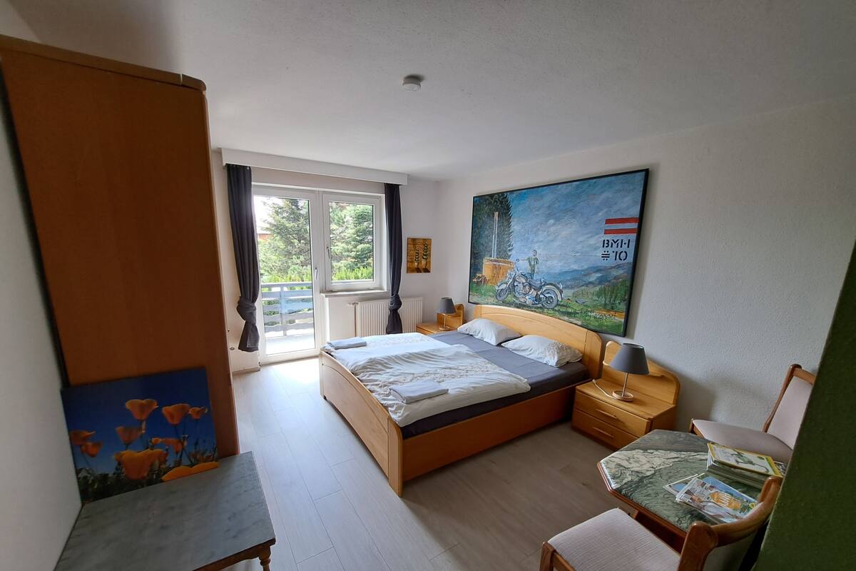 A bedroom with a bed, bedside tables, a chair, a desk, and a painting on the wall.