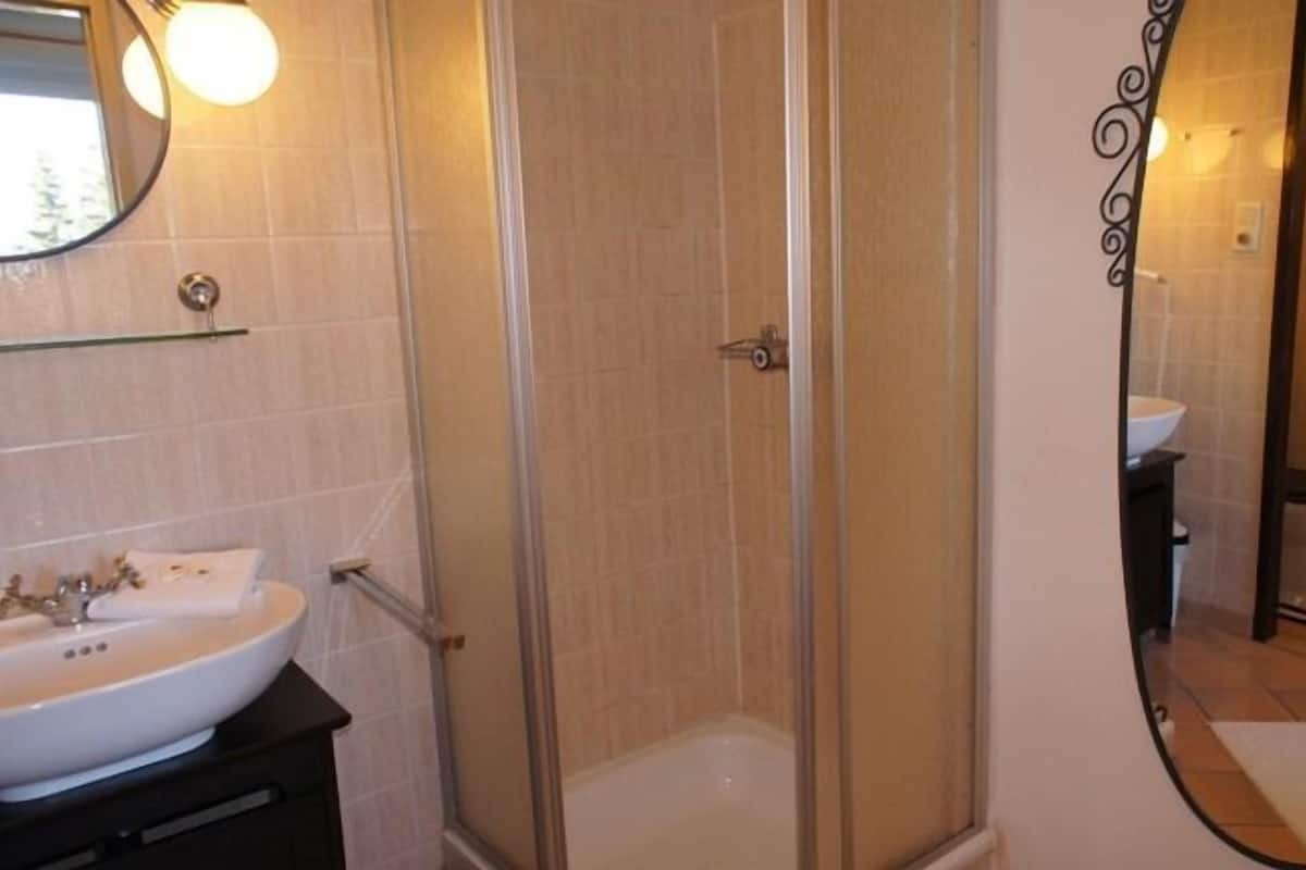 A bathroom with a glass-enclosed shower, a white sink, and a mirror with a decorative frame.