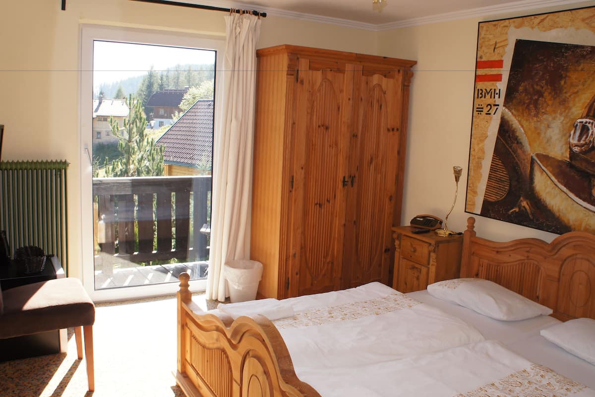A bedroom with a wooden bed, a nightstand, a chair, a television, and a large window with a view of a house and trees.