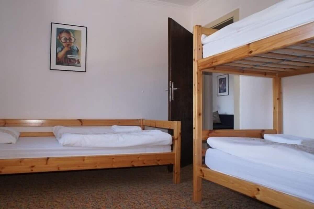 A room with two wooden bunk beds, a door, a framed picture on the wall, and a carpeted floor.
