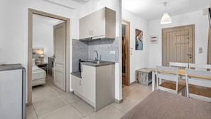 A compact kitchen with a central island, a dining area with a bench, and a small table. - Erato Hotel (Hersonissos)
