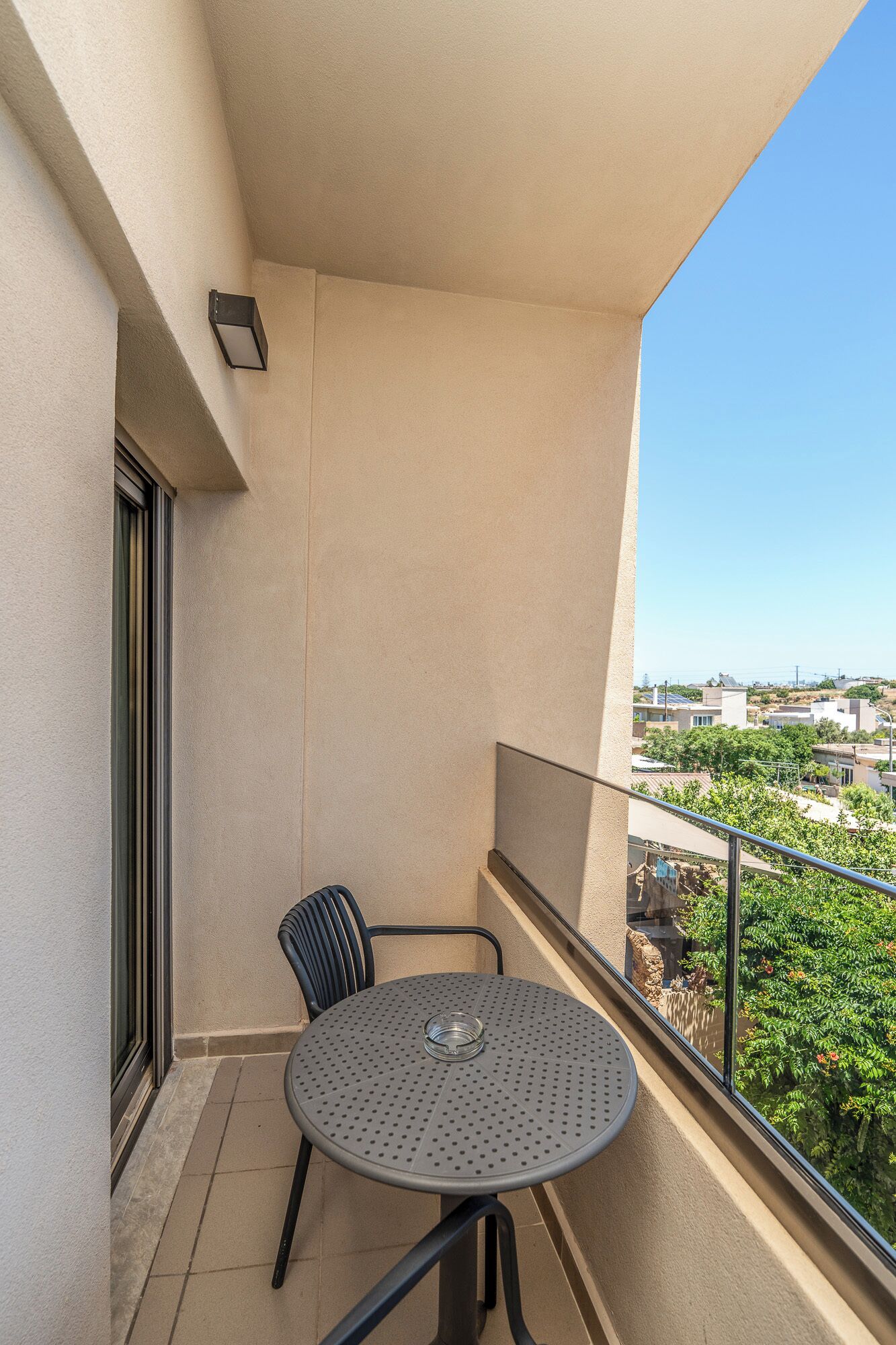 A balcony with a round table and chairs, a window, and a view of a residential area.