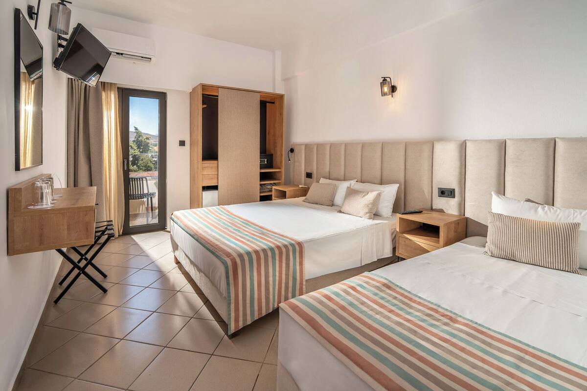Une chambre d’hôtel avec deux lits, un bureau, une chaise, une télévision et un balcon.