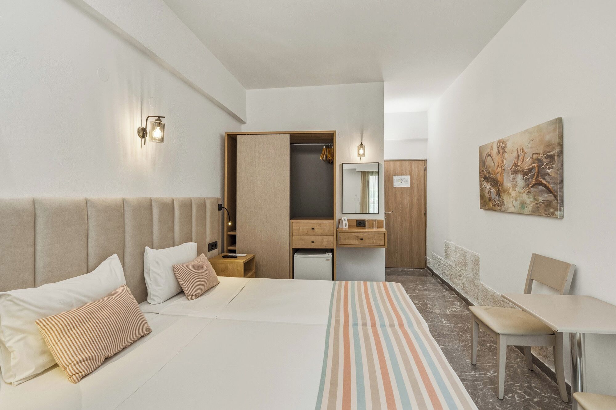 Ein Hotelzimmer mit Bett, Nachttisch, Schreibtisch, Stuhl, Kleiderschrank und einem Bild an der Wand.