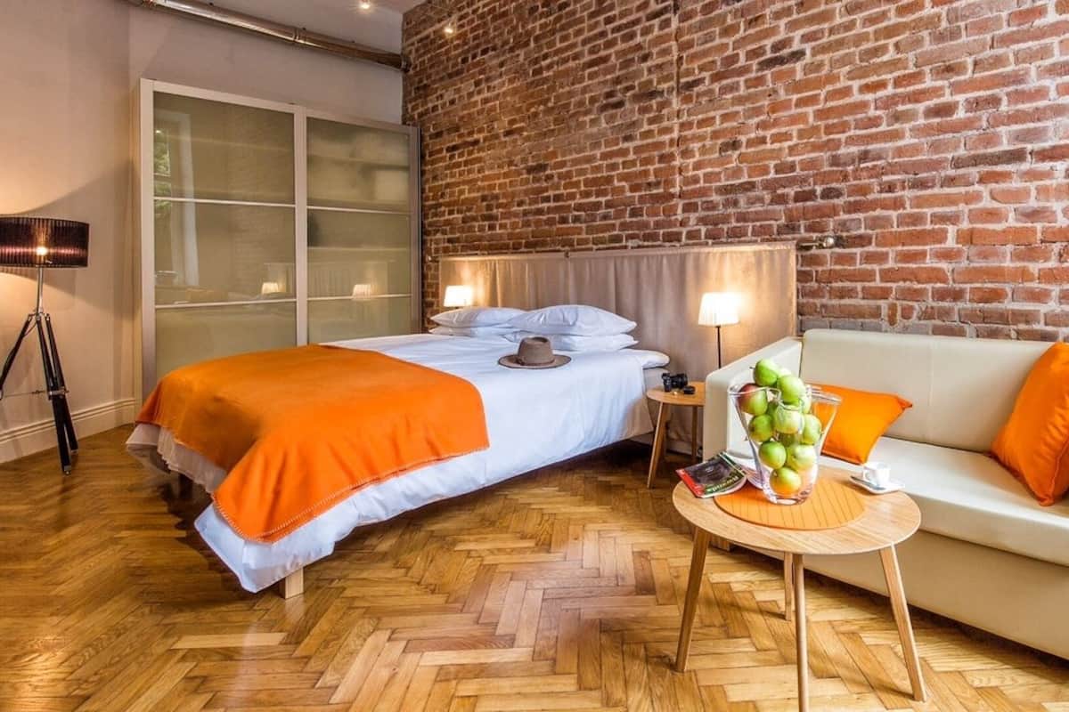 A hotel room with a bed, a sofa, a small table, and a brick wall.