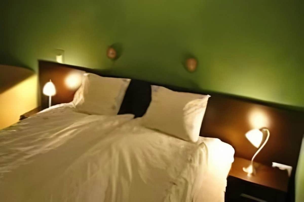 A neatly made bed with white linens, two bedside lamps, and a green wall.
