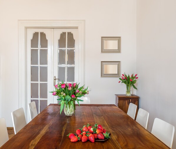 A dining room with a wooden table, white chairs, a vase of flowers, and a mirror on the wall.