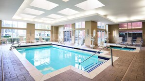 An indoor swimming pool with clear blue water, sunlit ceiling, and multiple lounge chairs around the pool area. - Hyatt House Seattle/Bellevue (Bellevue)