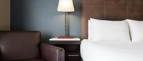 Una habitación de hotel con una cama, una mesita de noche, una lámpara y un sillón de cuero.