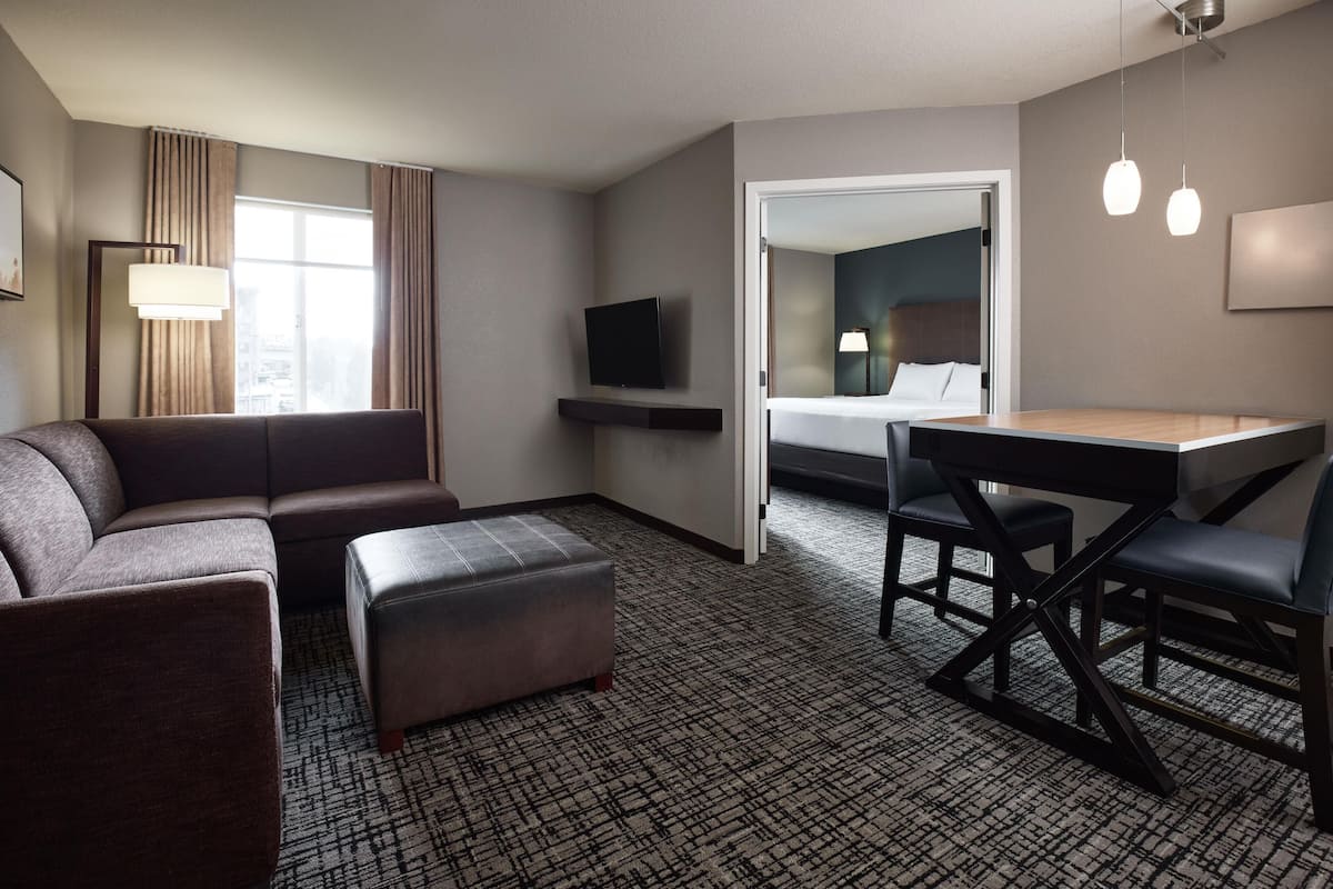 A hotel room with a sofa, ottoman, desk, and television.