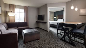 Une chambre d’hôtel équipée d’un canapé, d’un pouf, d’un bureau et d’une télévision.
