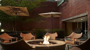 An outdoor seating area with wicker chairs, a fire pit, and two umbrellas. - Hyatt House Seattle/Bellevue (Bellevue)