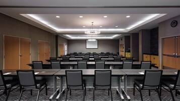 A conference room with multiple tables and chairs, a large screen, and a chandelier.