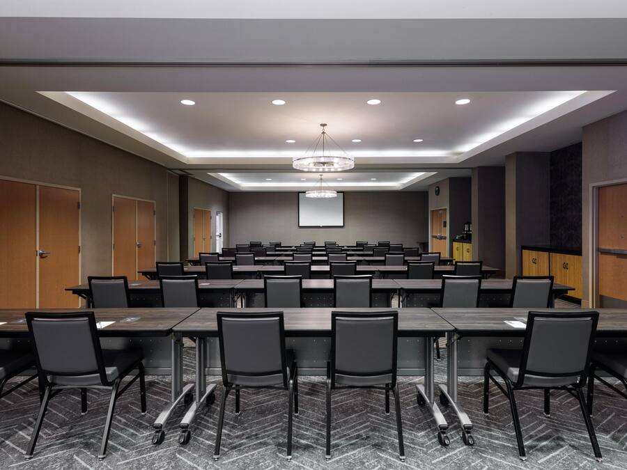 A conference room with multiple tables and chairs, a large screen, and a chandelier.