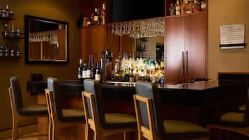 A bar area with wooden chairs, a bar counter, and shelves stocked with bottles and glasses.