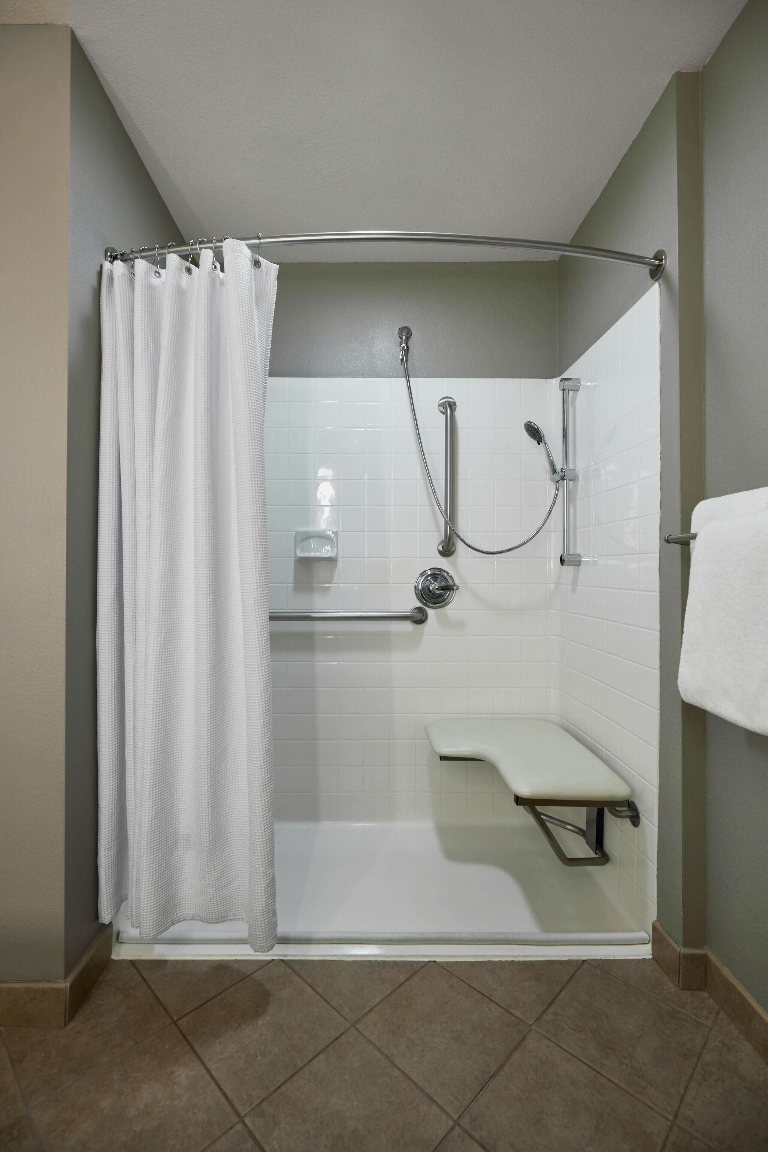 Un espace douche avec un rideau de douche blanc, une douchette à main et un banc.