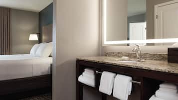 A hotel room with a bed, a bathroom with a sink, and a large mirror.