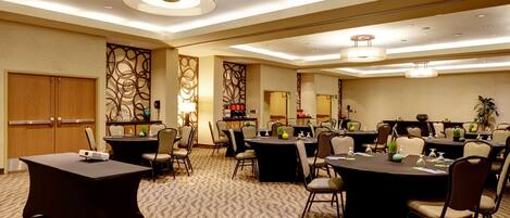 A conference room with multiple tables and chairs, equipped with presentation screens and a large mirror on the wall.