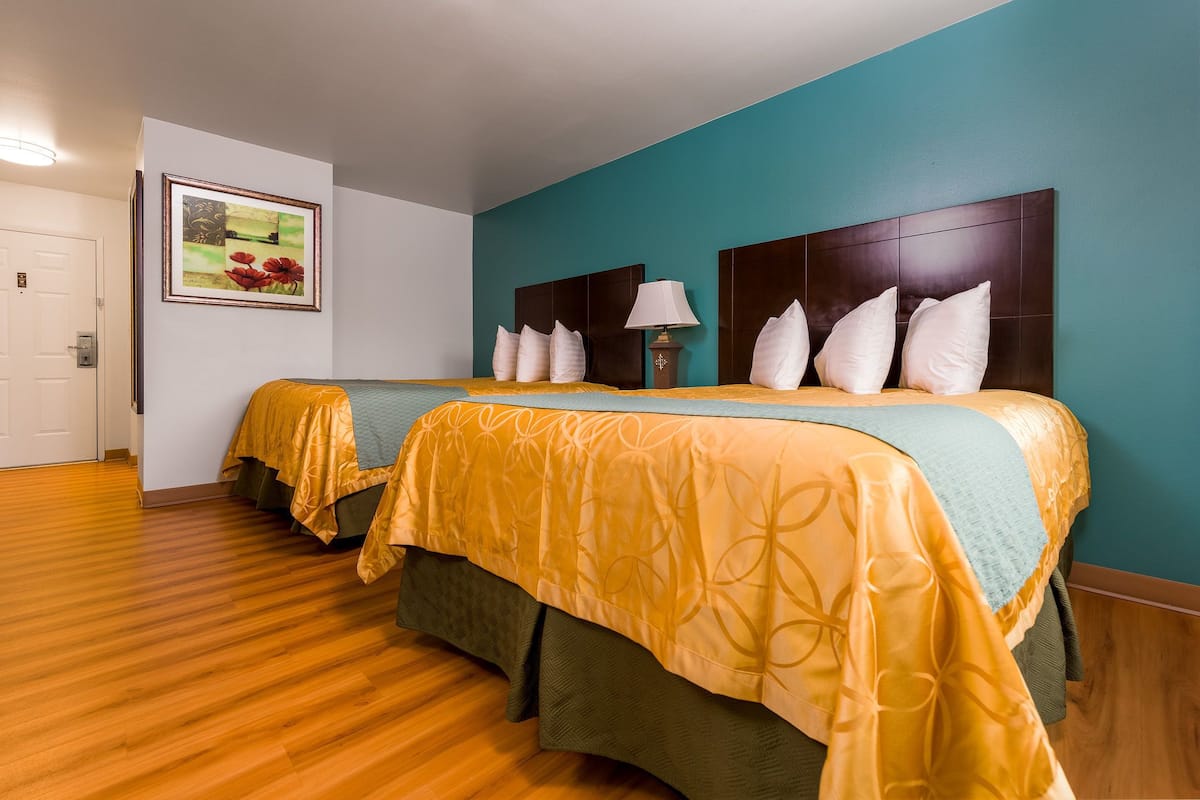 A hotel room with two beds, a teal wall, wooden flooring, and a framed picture on the wall.
