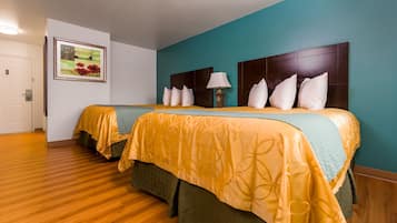 Ein Hotelzimmer mit zwei Betten, einer türkisblauen Wand, Holzboden und einem gerahmten Bild an der Wand.