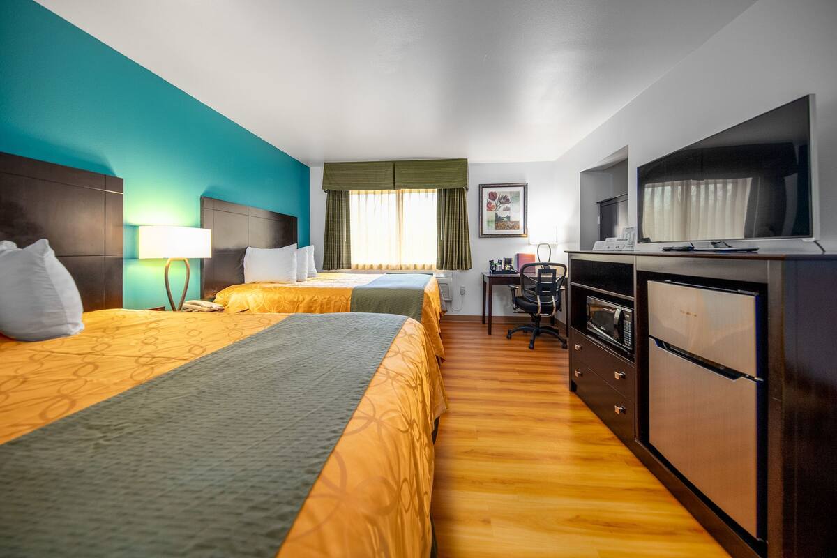 A hotel room with two beds, a desk with a computer, a microwave, and a refrigerator.