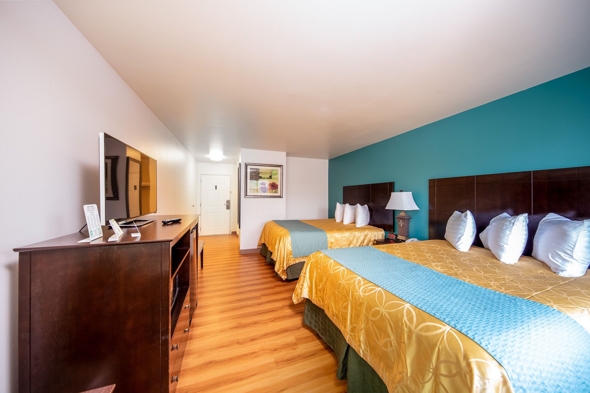 A hotel room with two beds, wooden flooring, a desk with a computer, and a large mirror.