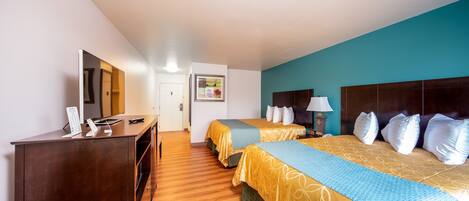 A hotel room with two beds, wooden flooring, a desk with a computer, and a large mirror.