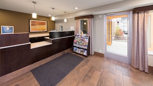 A reception area with a dark wooden reception desk, a framed artwork above it, and a magazine rack to the right. - Sunset Motel Hood River (Hood River)