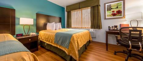 A hotel room with two beds, a desk, a chair, a clock, and a window with curtains.