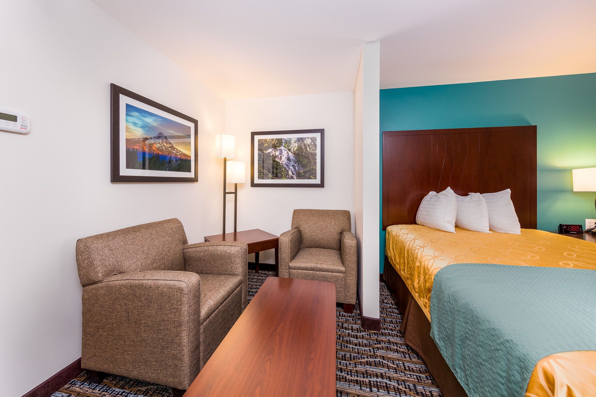 A hotel room with a bed, two armchairs, a small table, and two framed pictures on the wall.